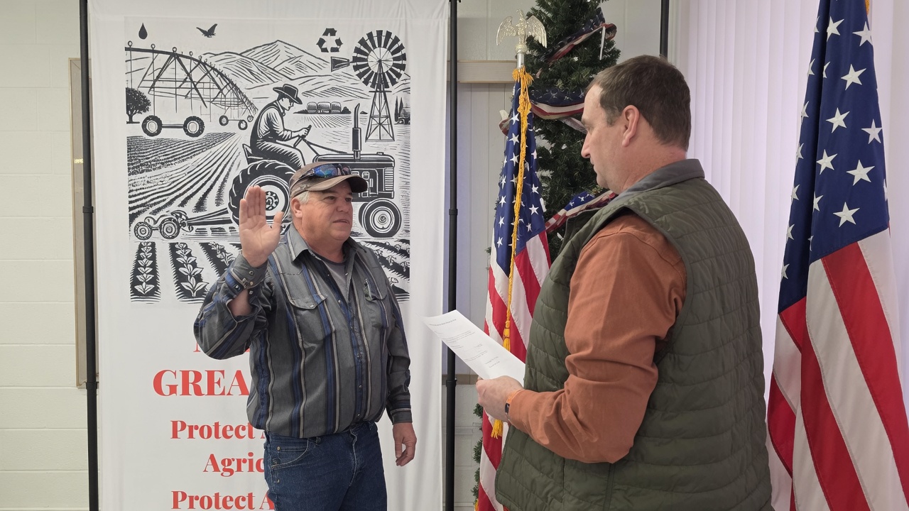 Fred Simon raising his right hand to take the oath of office as a Klamath Irrigation District director, in front of the District’s agriculture banner and the American flag.